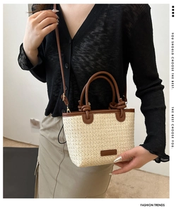 Close-up of beige woven straw tote with brown leather handles and adjustable strap