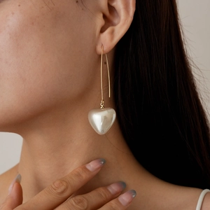 Detail of elegant gold drop earrings featuring a heart-shaped pearl on female model