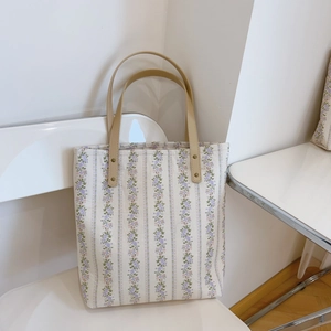 Floral purple tote bag with khaki handles and vertical stripes in a clean interior setting