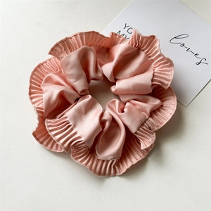 Detail of light pink pleated satin scrunchie with soft ruffled edges on a beige background