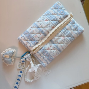 Blue floral quilted makeup bag with heart pendant and ribbon strap on a beige background