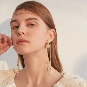 Detail of long gold tassel earrings with pearls worn by a model in elegant lighting