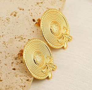 Detailed shot of golden sun hat stud earrings with bow tie on travertine stone base