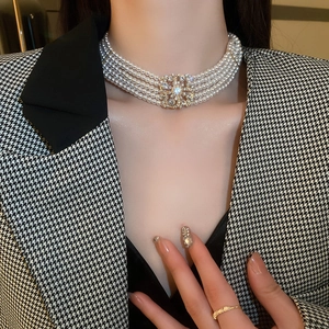 Detailed view of layered pearl necklace with crystal flower clasp on model in blazer