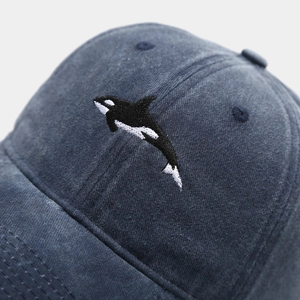 Close-up of high-density orca whale embroidery on washed blue cotton baseball cap