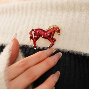 Detail of a vintage red enamel horse brooch with sparkling rhinestones on soft fabric