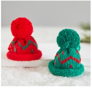 Close-up of mini knitted Christmas hats in red and green colors on a snowy background