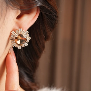 Détail de boucles d'oreilles soleil en or champagne et cristaux portées par le mannequin