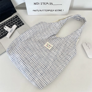 Détail du sac cabas en toile à carreaux bleus et blancs avec étiquette sur bureau blanc