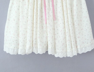 Détail de l'ourlet de robe à fleurs avec broderie dentelle et cordon rose à carreaux