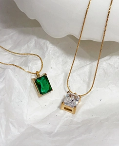Macro view of gold snake chain with emerald green and clear rectangle cut zircon pendants