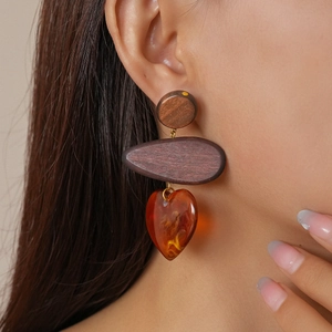 Close-up of ethnic wood and amber resin heart drop earrings worn by a model