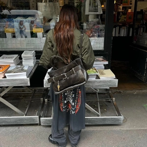 Street style shot of a dark coffee leather shoulder bag with a buckle strap and key pendant