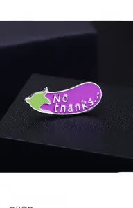 Macro shot of purple eggplant enamel pin with No thanks... text on black leather surface