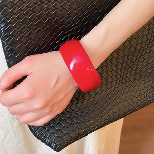 Polished red acrylic wide bangle bracelet styled with a black woven leather clutch bag