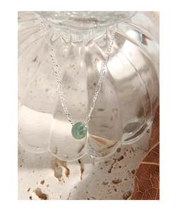 Macro view of a S925 silver chain with a green jade pendant over a glass bottle