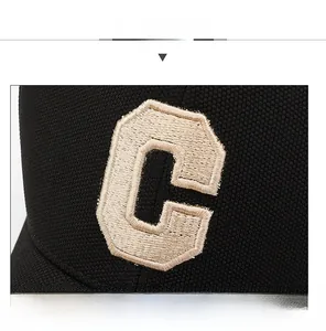 Close-up of beige C letter embroidery on black textured fabric baseball cap