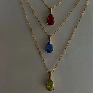 Detailed close-up of water drop gemstone pendants in red, blue, and lime green on gold chains