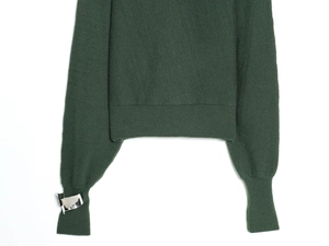 Détail des manches du pull en maille vert foncé avec boucles métalliques argentées décoratives