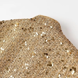 Dettaglio macro di paillettes dorate su tessuto tweed con filato metallico intrecciato
