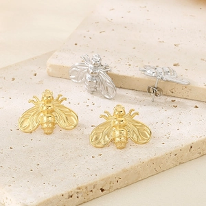 Macro shot of bee stud earrings in gold and silver finish on a stone base