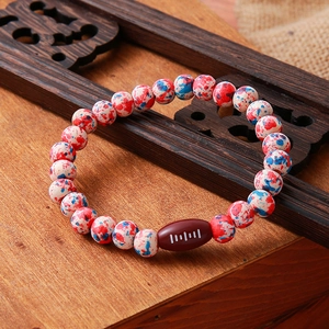 Detail shot of the elastic beaded bracelet with a brown football charm on a wood tray