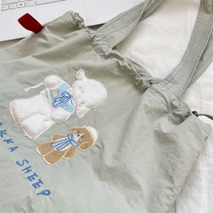 Detail of embroidered sheep and puppy design on light green canvas tote bag with drawstring