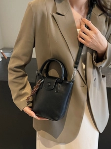 Minimalist black leather bucket bag with top handle and tassel charm worn with a blazer