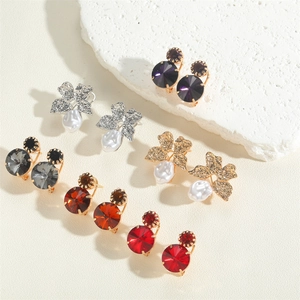Flat lay of multiple acrylic flower drop earrings and crystal studs on a stone texture