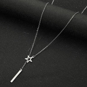 Close-up of minimalist silver necklace with star and vertical bar pendants on black texture