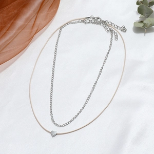 Close-up of a double-layer heart pendant necklace on a white silk and eucalyptus leaf background