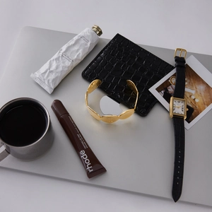 Set con bracciale dorato, portafoglio in pelle nera e orologio vintage su uno sfondo laptop
