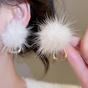 Detail view of fluffy white pompom earrings with elegant gold triangular metal clasp