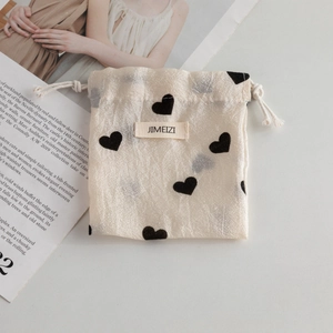 Detail of satin champagne drawstring storage bag with black heart patterns and woven label