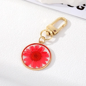 Detail of a golden keychain with a real red daisy preserved in a transparent resin pendant