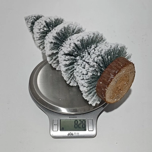 Miniature cedar Christmas tree with white flocking on a scale weighing 82.8 grams