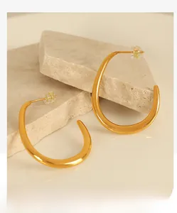 Macro detail of golden geometric curved earrings placed on natural beige stones
