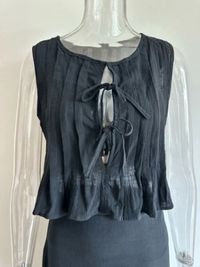 Detail of black pleated sleeveless top featuring front tie bows and breathable fabric