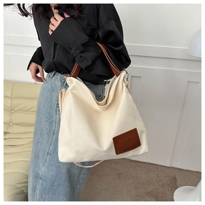 Detail of canvas tote bag with brown leather handles and decorative brand patch