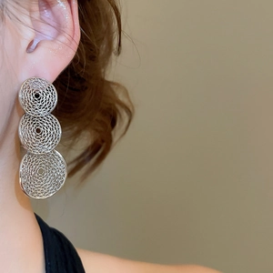 Close-up of tiered hollow silver drop earrings with intricate filigree on a female model