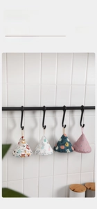 Detail of four triangular cotton oven mitts hanging on hooks against white tiles