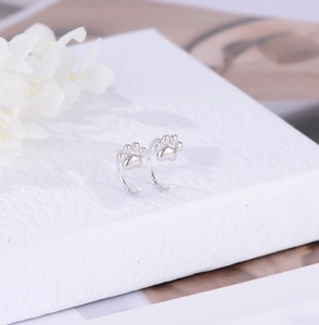 Macro detail of silver cat paw earrings on a white gift box with floral accents