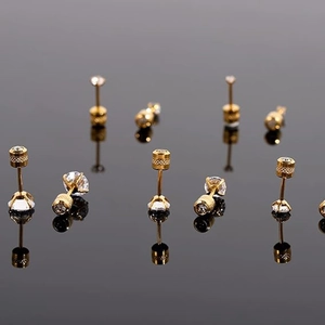 Close-up of five pairs of golden stud earrings with clear zircon stones on a reflective surface
