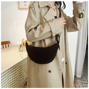 Detail of adjustable black corduroy crescent crossbody bag styled on a beige trench coat