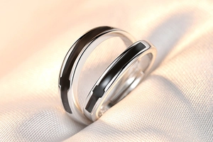 Close-up of silver couple rings with black inlay design on textured fabric background