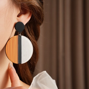 Détail de boucles d'oreilles rondes avec grain de bois et motifs acryliques rayés