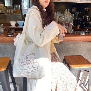 Close-up of white plush tote bag featuring embroidered brown bears and text detail
