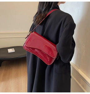 Detail of burgundy patent leather shoulder bag with adjustable strap worn on woman's shoulder