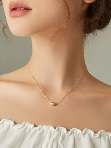 Close-up of minimalist gold bean pendant necklace worn by a model in warm lighting