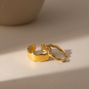 Set of minimalist 18K gold-plated wave-shaped open rings on a stone surface